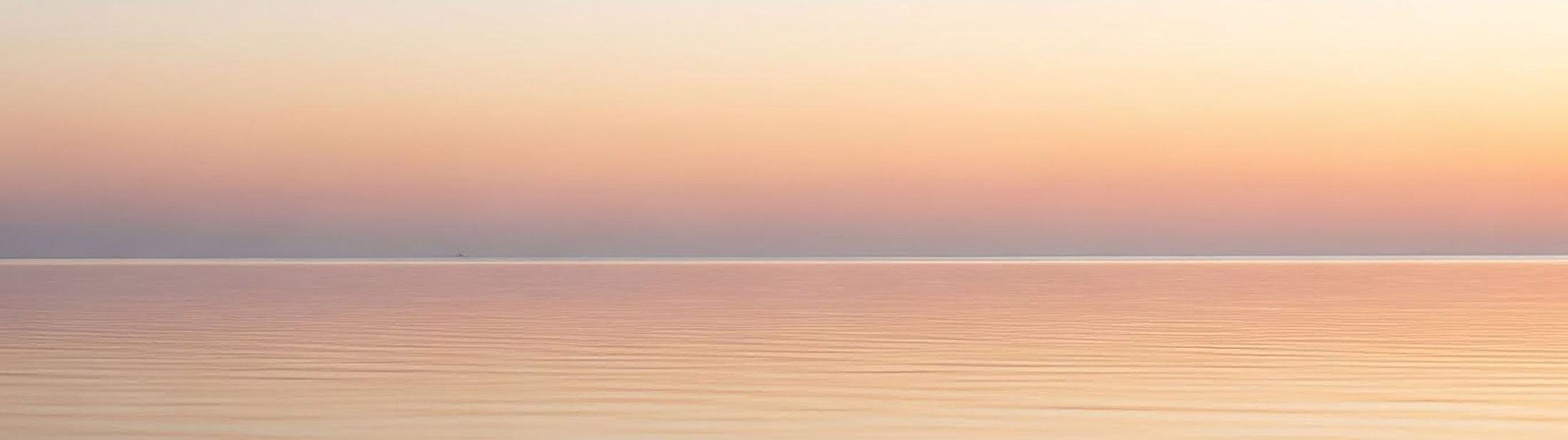 A pastel dawn sky over calm water, the horizon centered and still